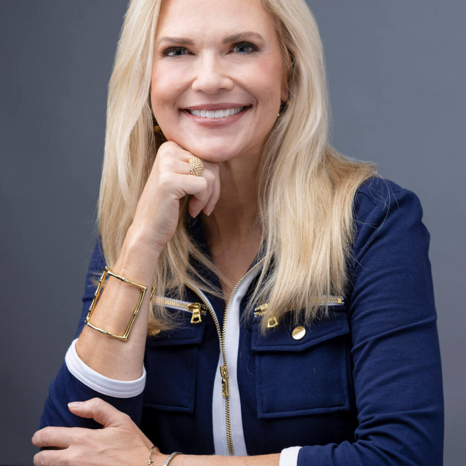 Professional Headshot of Blonde Women in Blue Blazer With White Accents Sitting at A Table